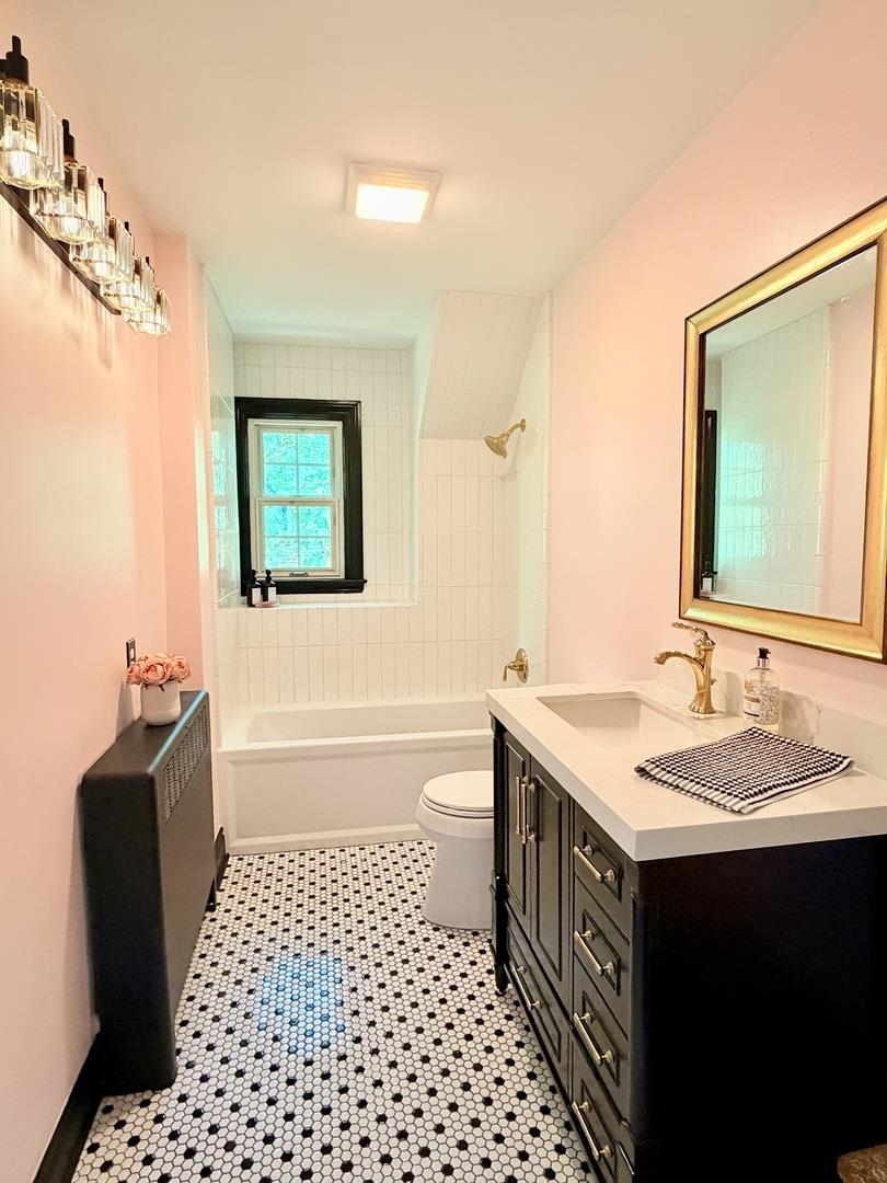 Bathroom with a black-trimmed window, white tub, dark vanity, brass fixtures, and patterned tile floor.