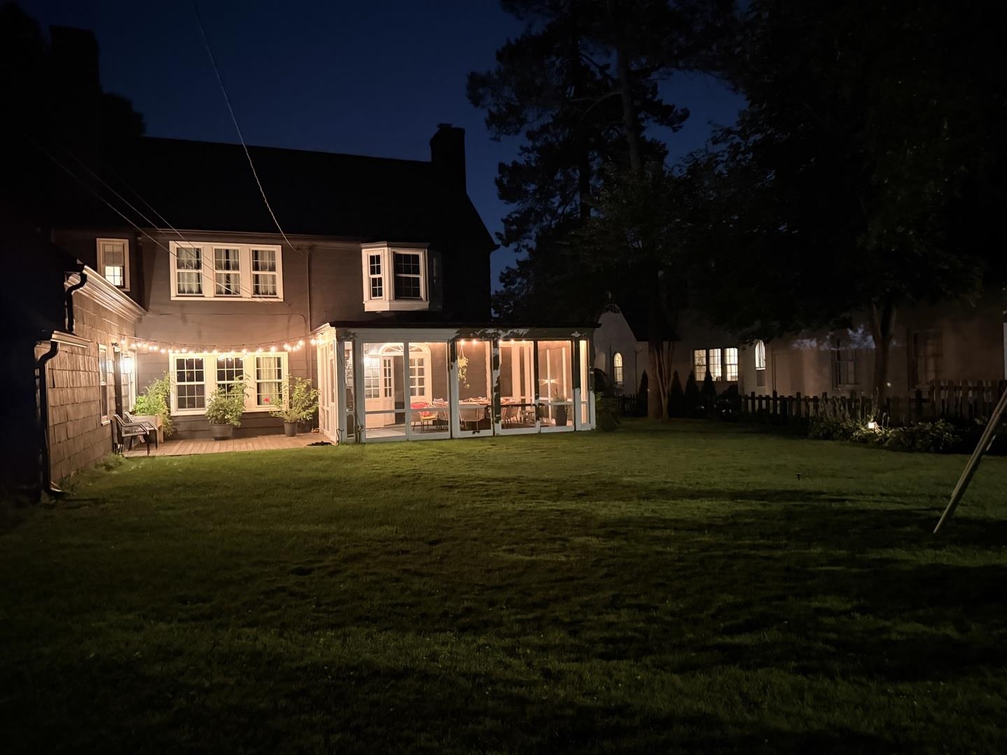 Two-story house at night with a warmly lit glass-enclosed porch and spacious lawn.