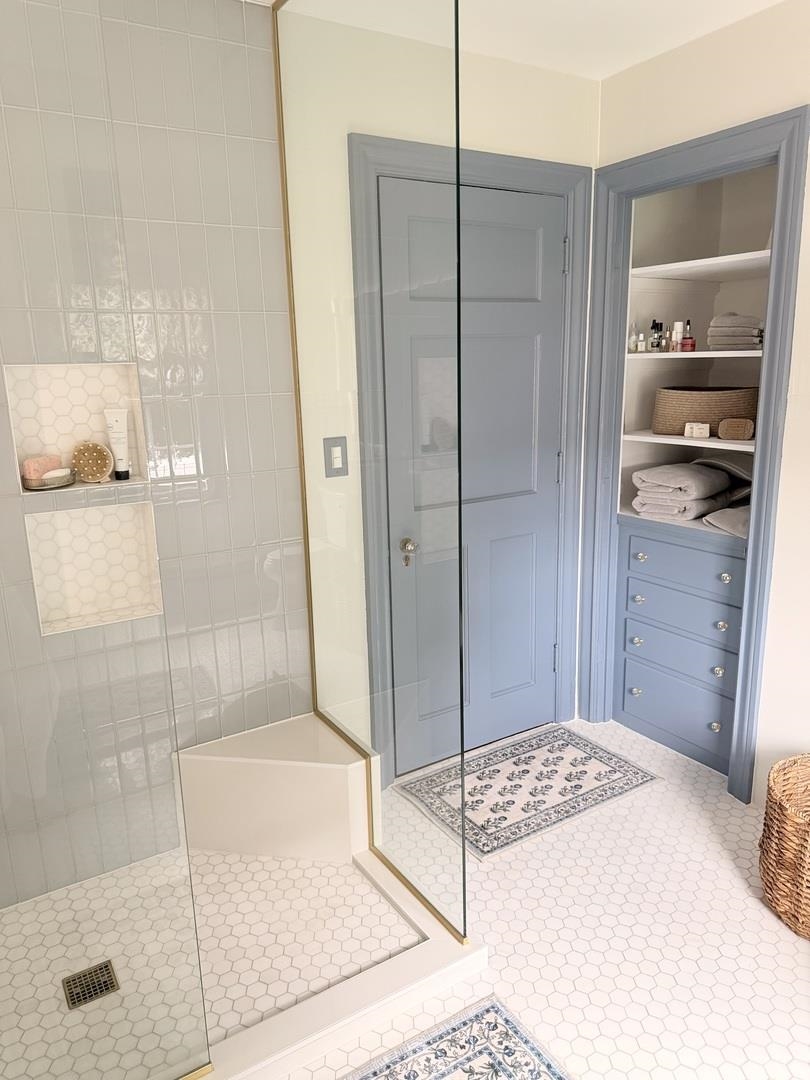 Bathroom with a glass walk-in shower and blue-gray built-in shelves stocked with folded towels.