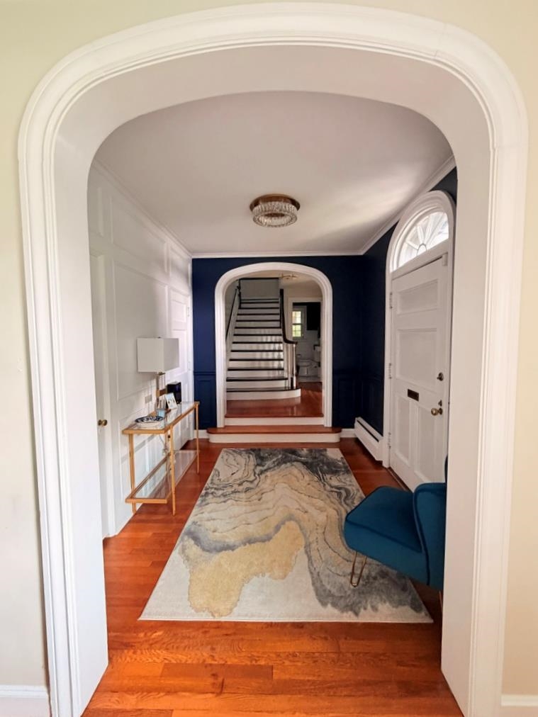 Entry hall with a white front door, patterned rug, and staircase beyond an arched opening.