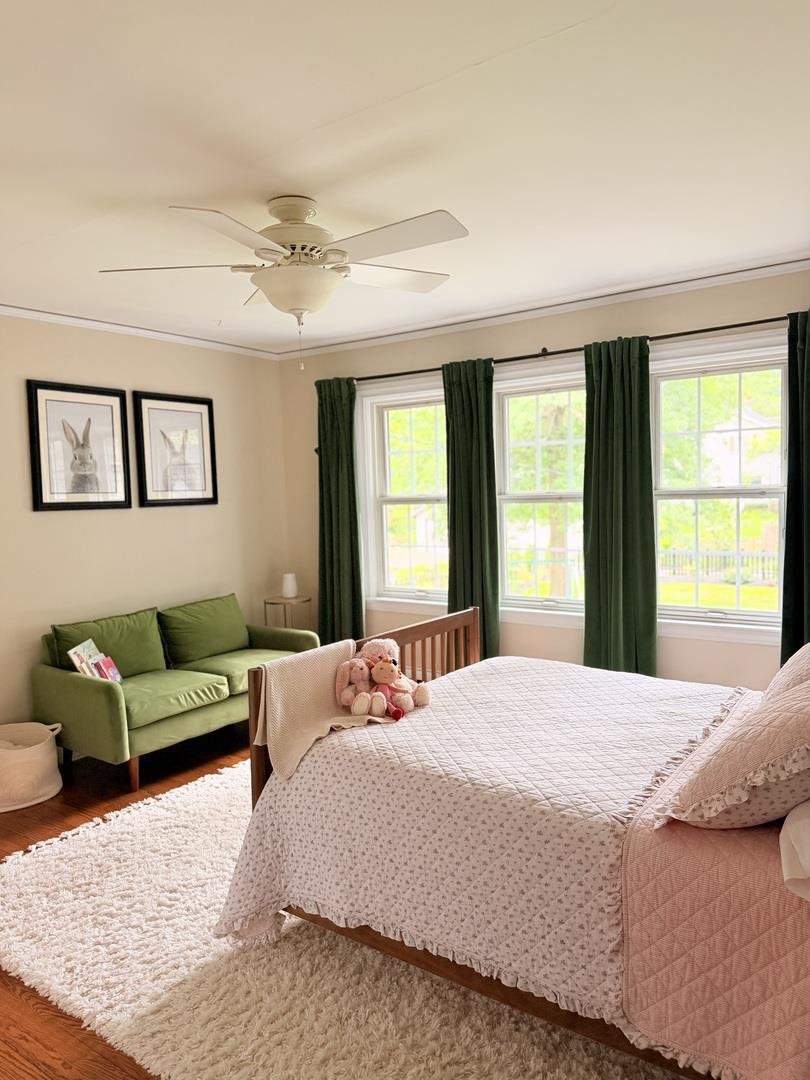 Bedroom with a pink-quilted bed, green loveseat, stuffed animals, and three sunlit windows.