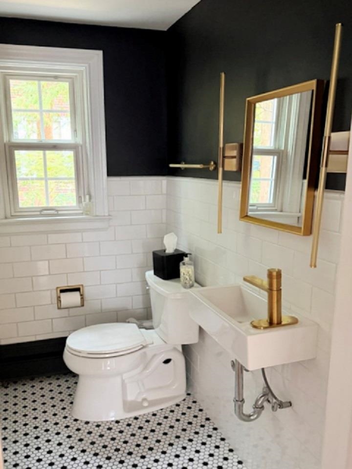 Bathroom with a wall-mounted sink, brass fixtures, gold-framed mirror, and black-and-white patterned floor.