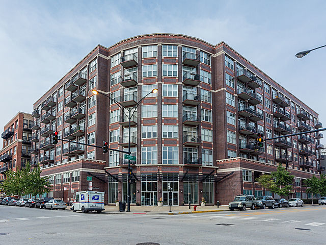 Urban apartment building with red brick, rows of balconies, and a rounded corner facade.