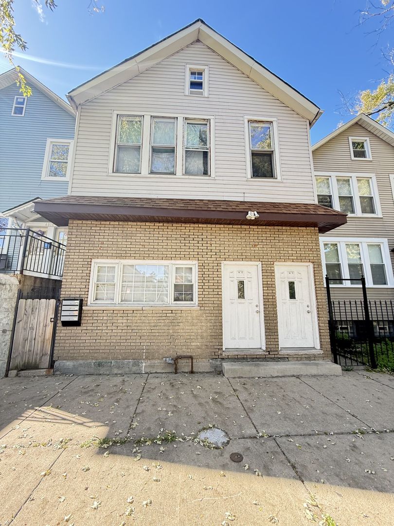 Two-story house with a tan brick lower level, two front doors, and a white-sided upper floor.