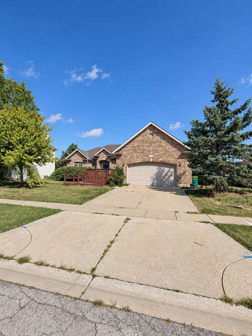 Brick house with a two-car garage, broad concrete driveway, and small wooden front deck.