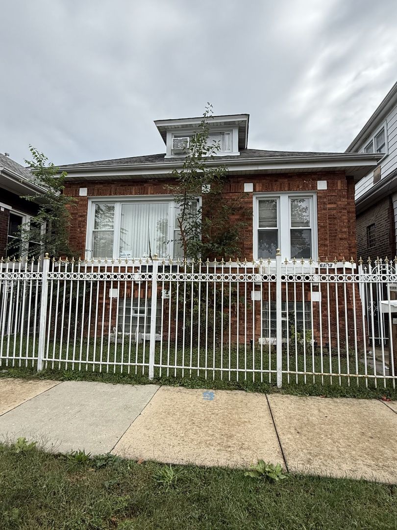 Red brick house with a roof dormer behind a white metal fence.