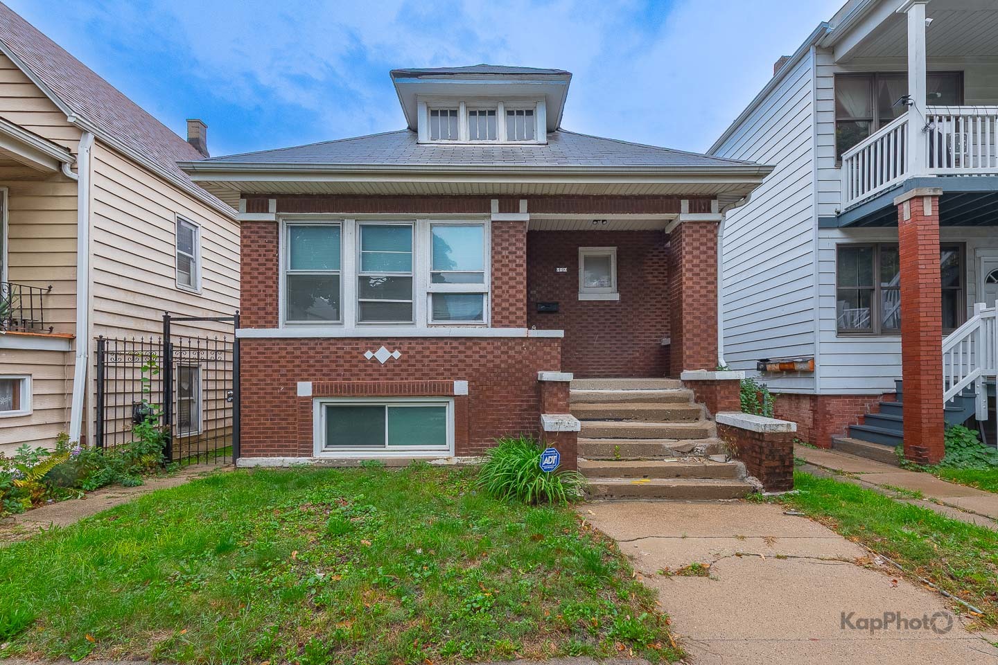 Red-brick bungalow with a front dormer, broad steps, and a small lawn.