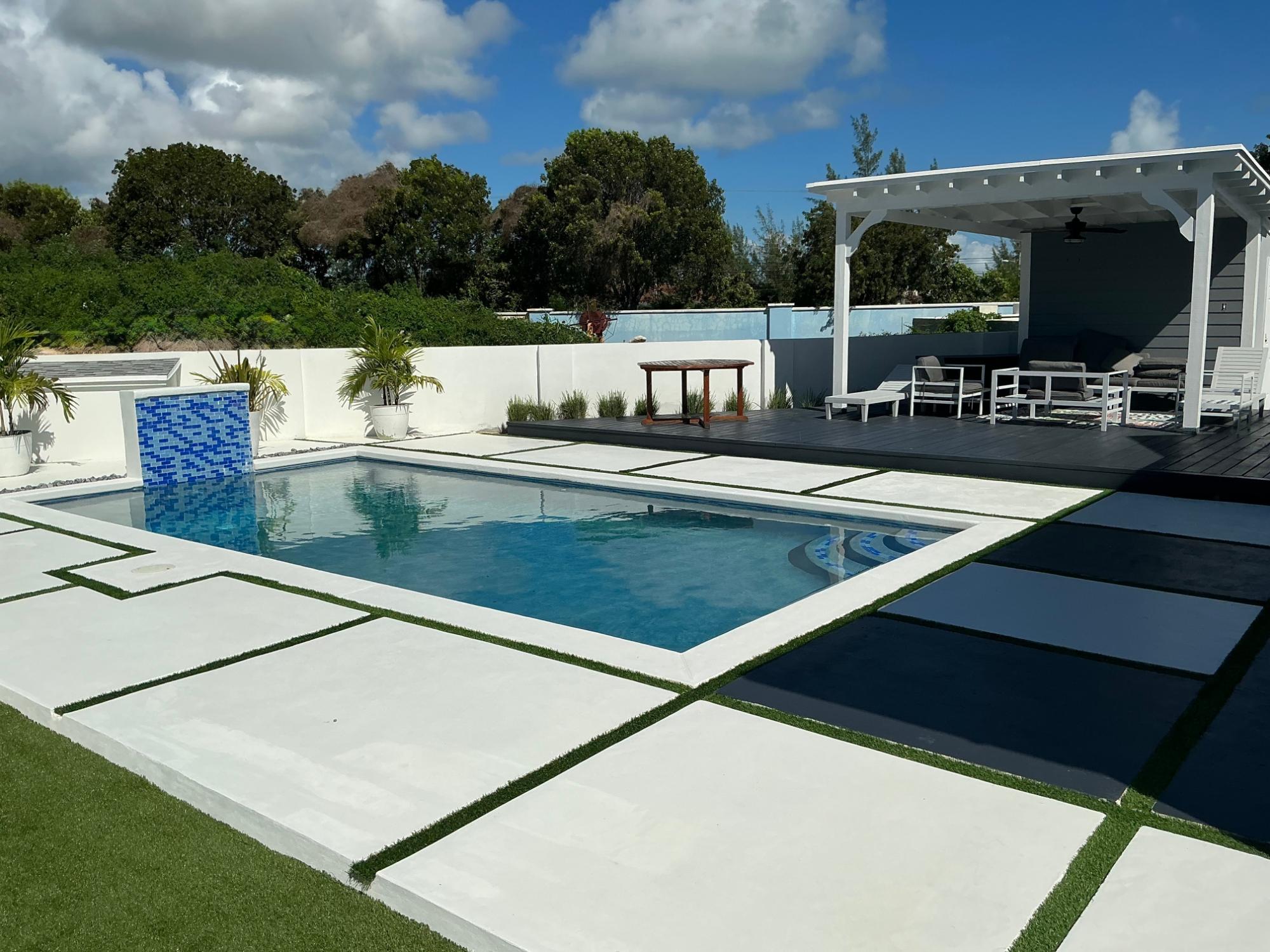 Outdoor pool with a blue-tiled water feature beside a covered patio and white geometric paving.