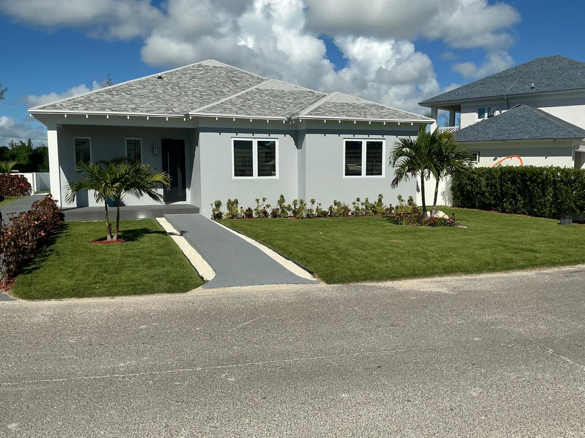 Gray single-story home with a shingled roof, palm trees, and a walkway across the lawn.