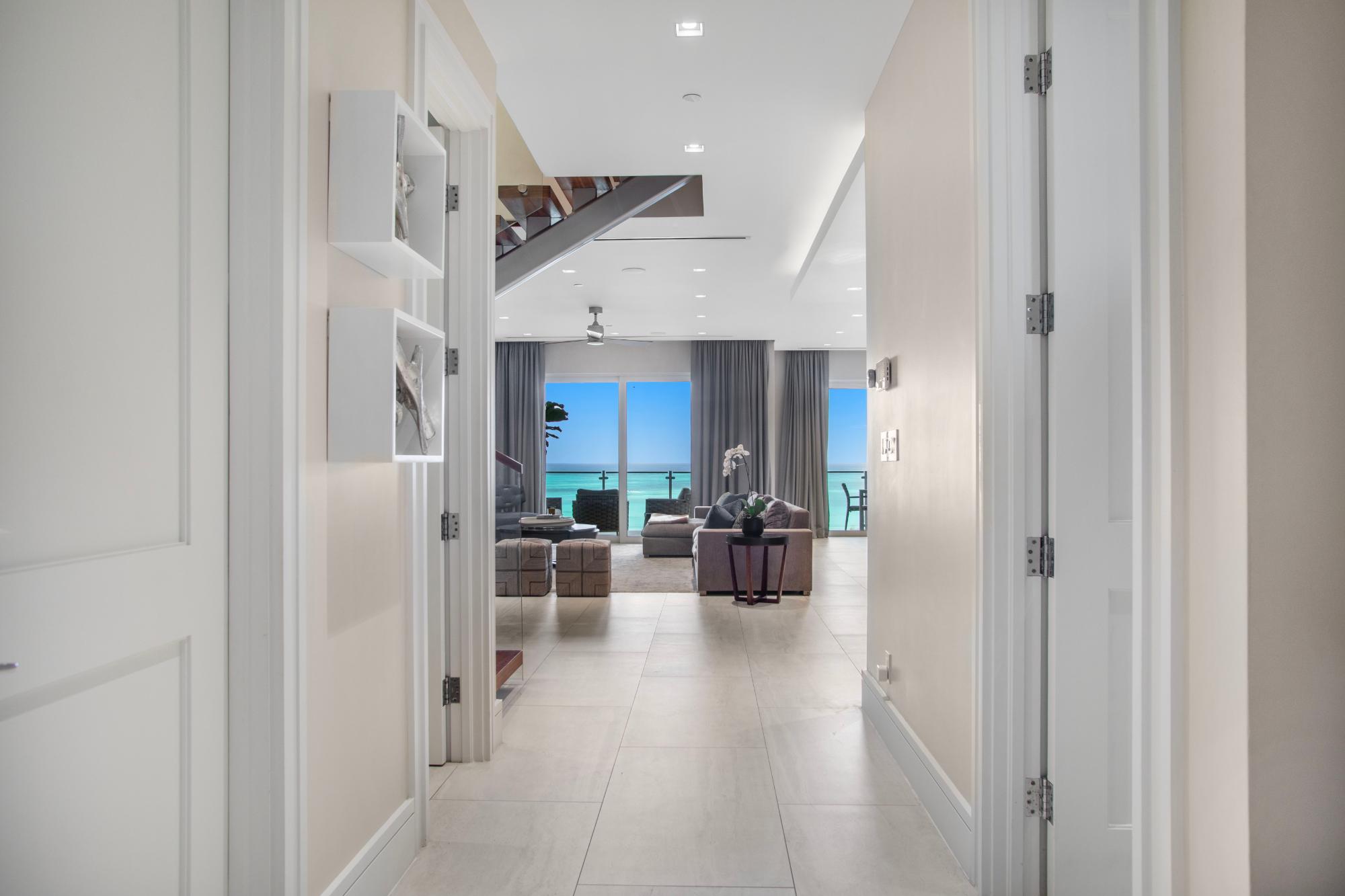 Hallway opening onto a furnished living room with floor-to-ceiling ocean views.