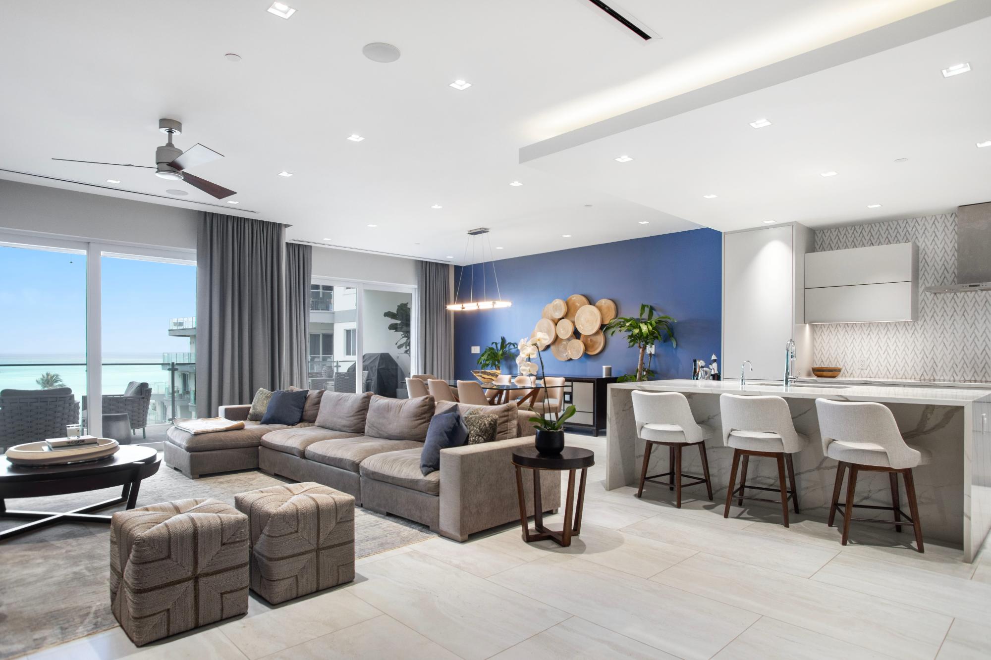 Open-plan living room and kitchen with a gray sectional, blue accent wall, and ocean views.