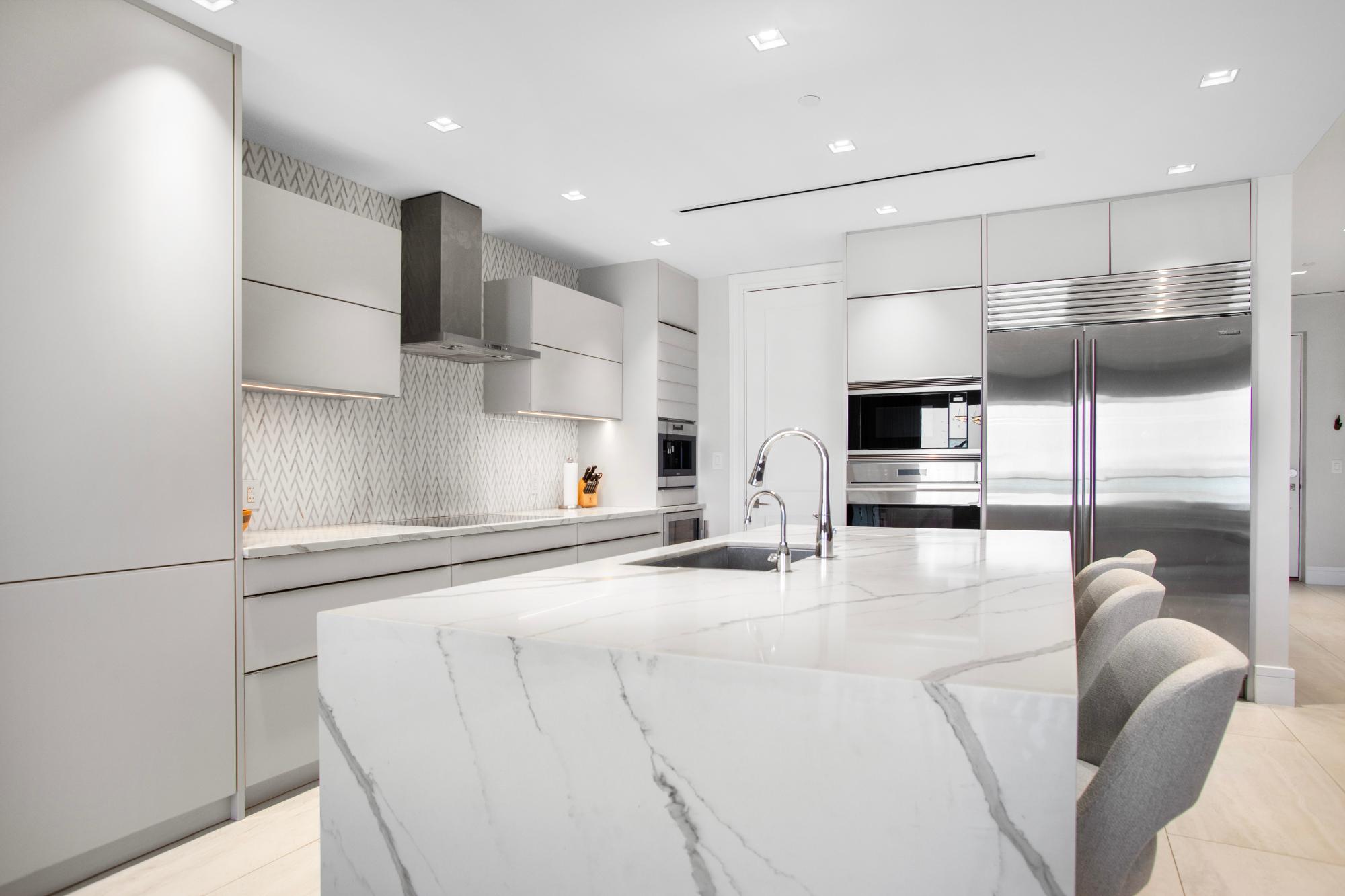 Contemporary kitchen with a veined white island, gray counter stools, and stainless steel appliances.