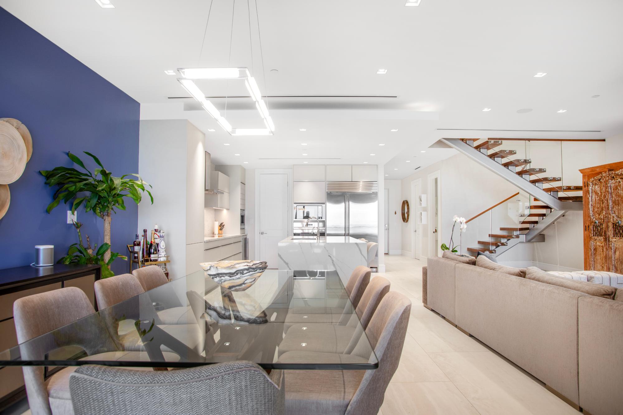 Open-plan penthouse dining and living area with a glass table, modern kitchen, and open staircase.