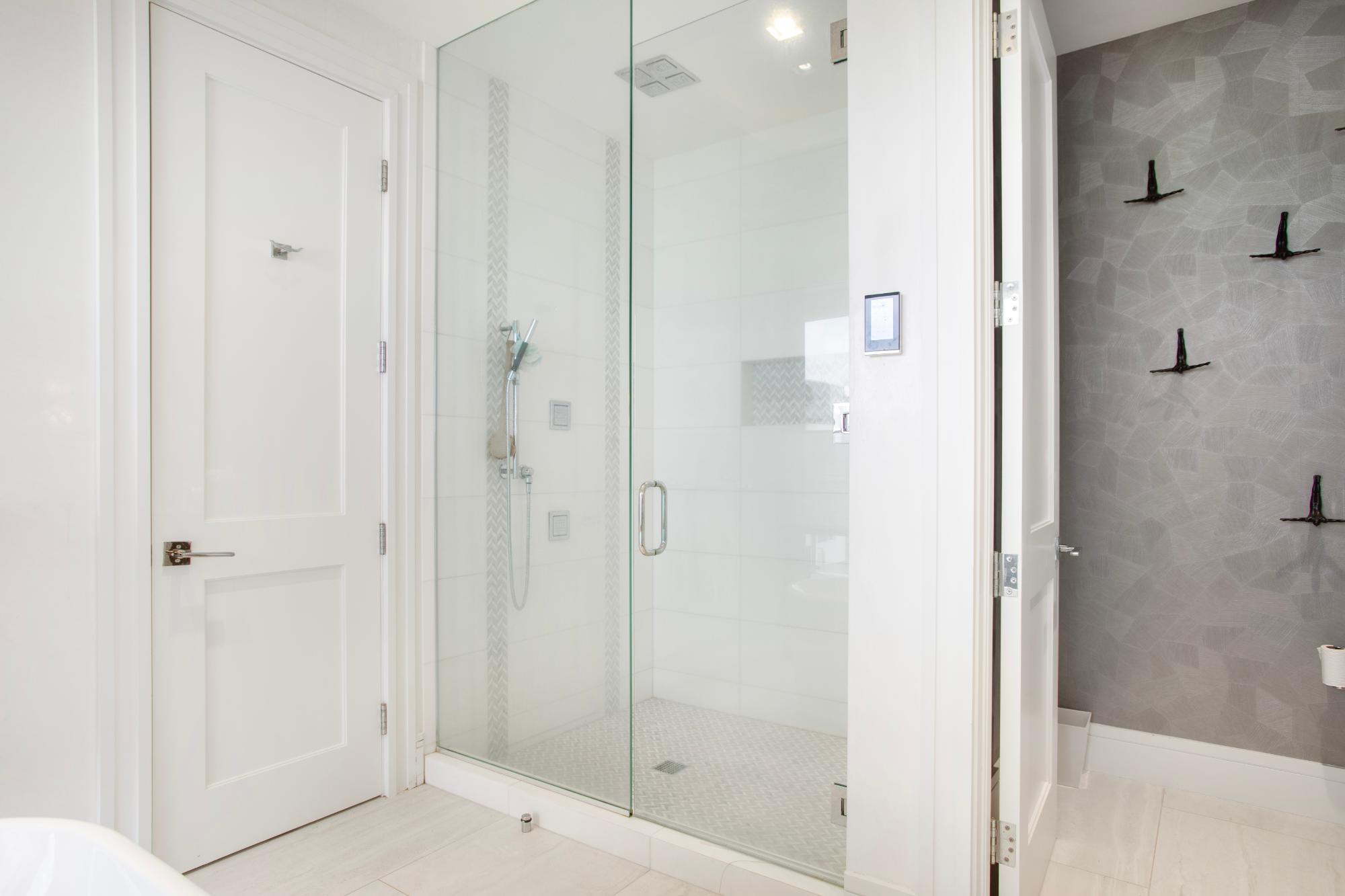 Modern bathroom with a glass walk-in shower and gray accent wall with black hooks.
