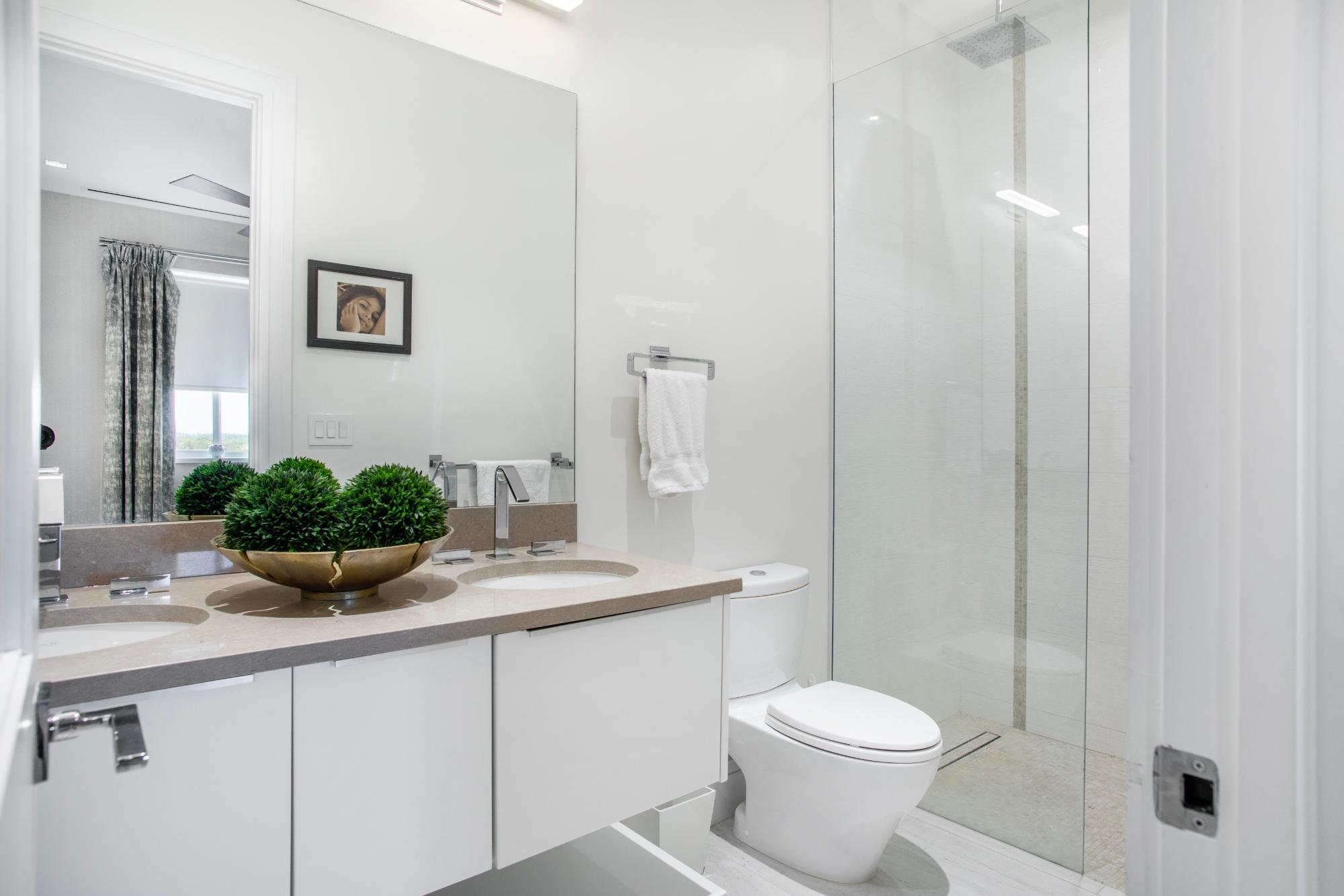 Modern bathroom with a double vanity, green plant arrangement, and glass-enclosed shower.
