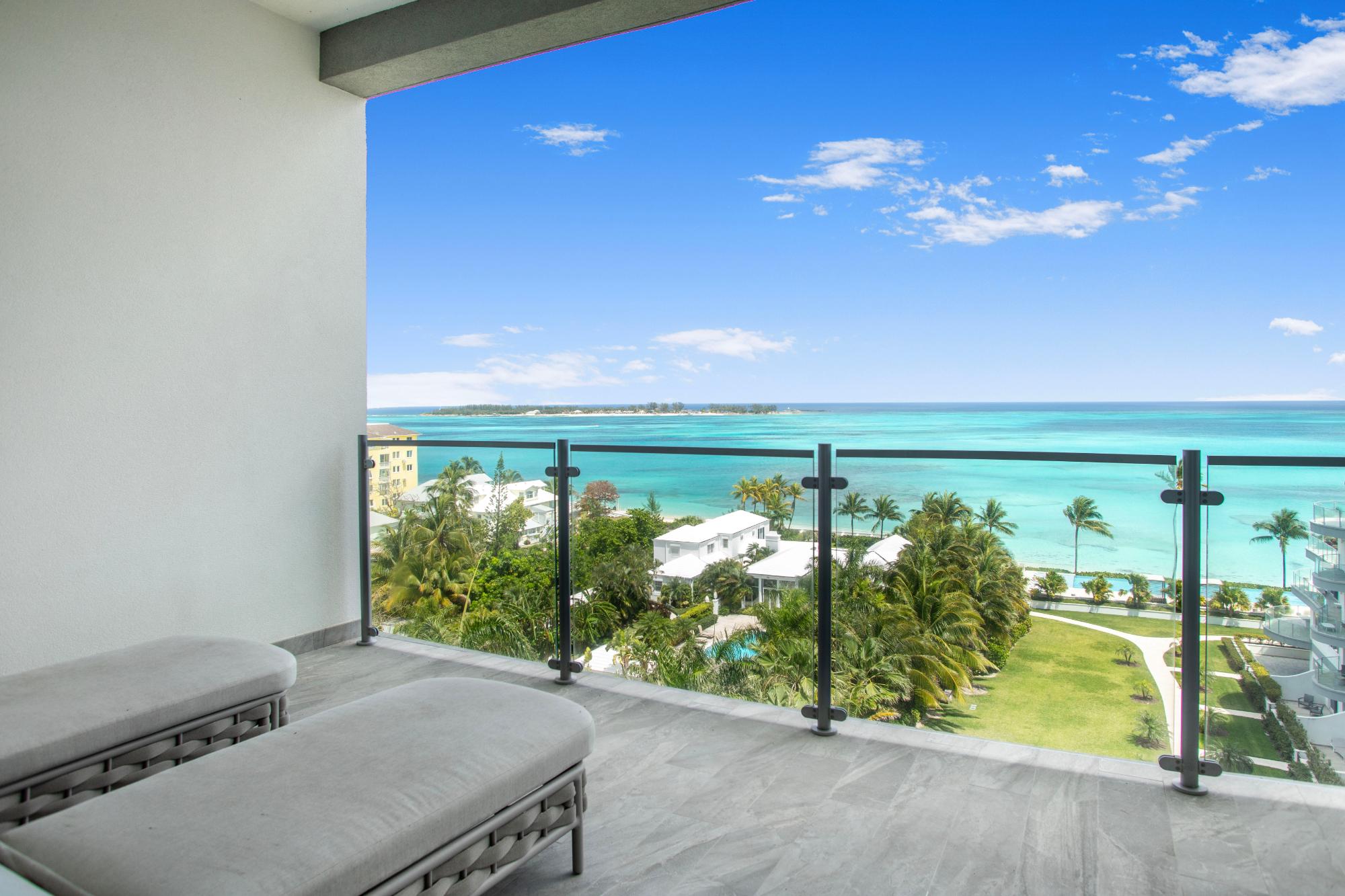 Balcony with gray loungers overlooking turquoise water and a palm-lined beachfront.