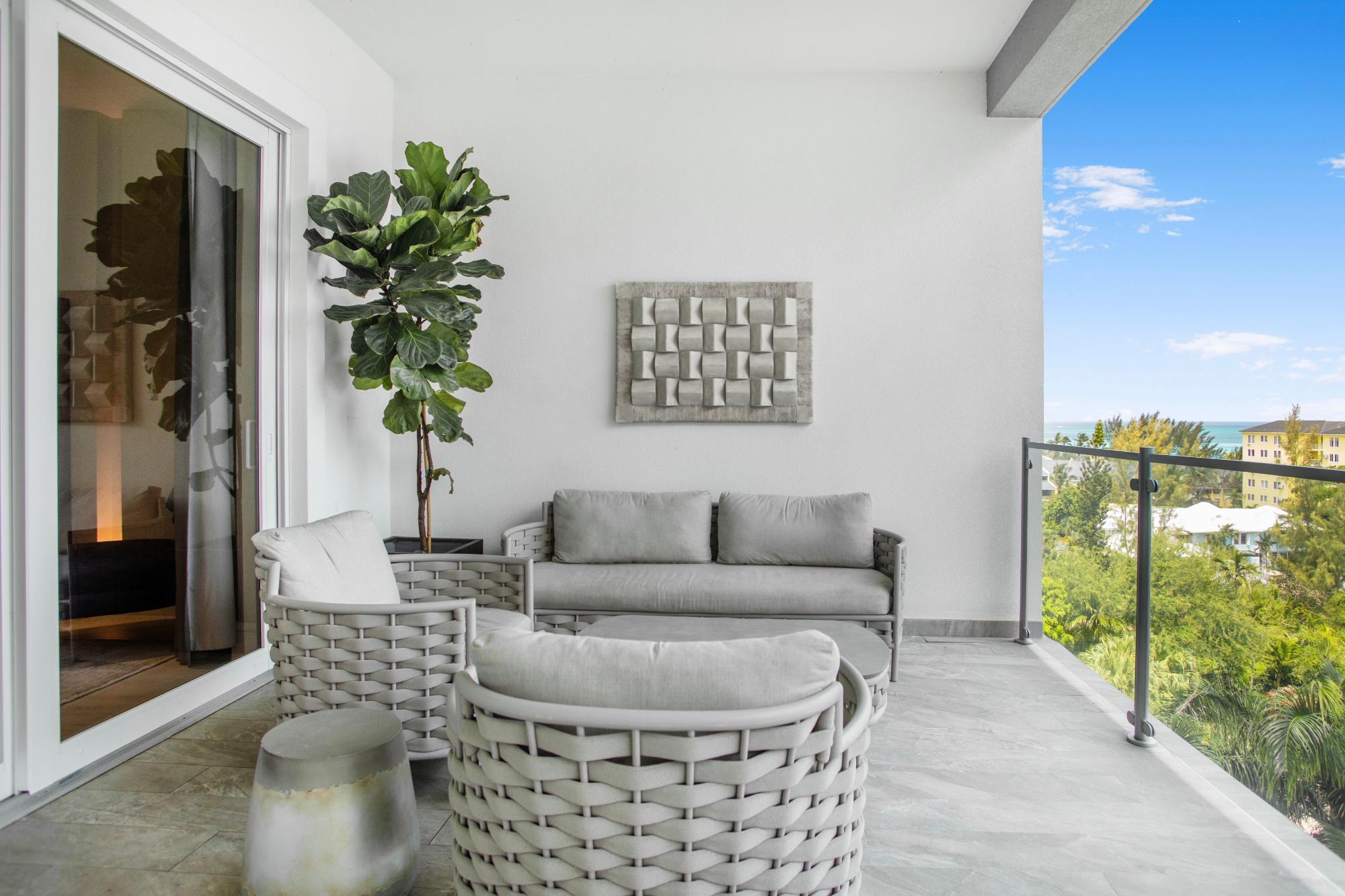 Condominium balcony with woven gray seating overlooking tropical greenery and turquoise water.