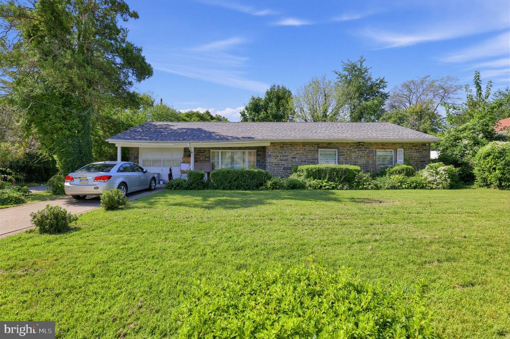 Single-story stone ranch home with a broad green lawn and a car in the driveway.