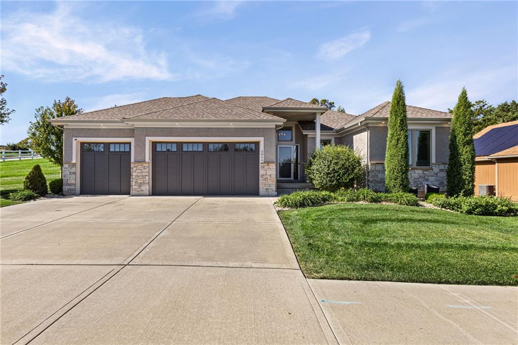 Single-story gray-and-stone home with a two-car garage, broad driveway, and landscaped lawn.