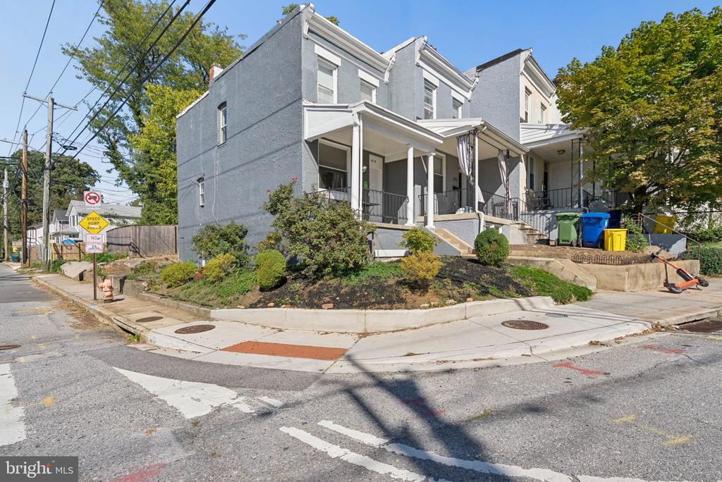 Attached gray homes with covered porches and shrubs on a landscaped corner lot.