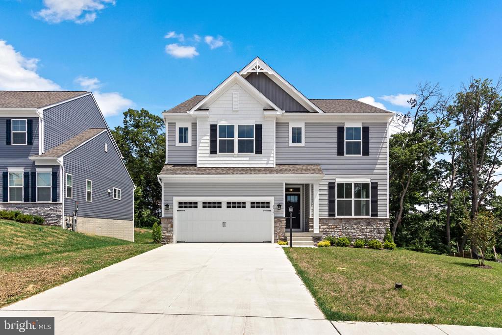 Two-story gray house with black shutters, stone accents, and a wide driveway.