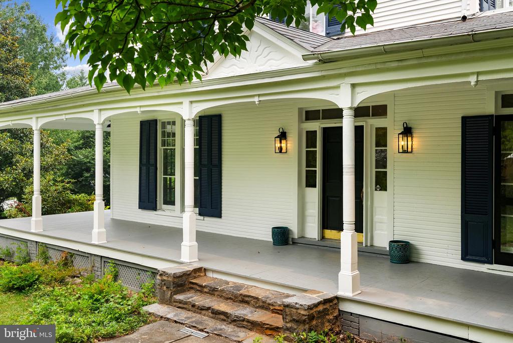 White house with a broad columned porch, dark shutters, and stone front steps.