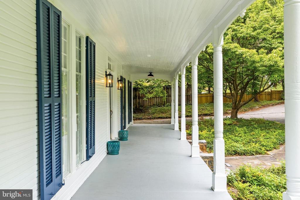 Covered front porch with white columns, navy shutters, and turquoise planters overlooking a leafy yard.