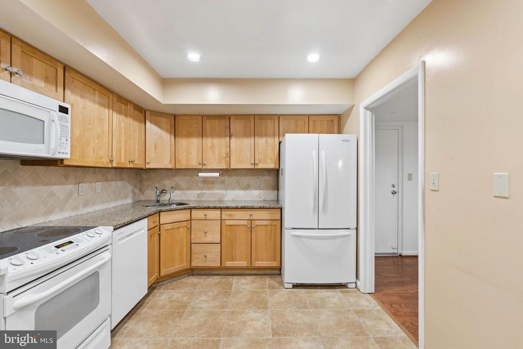 Kitchen with light wood cabinetry, granite counters, white appliances, and beige tile flooring.