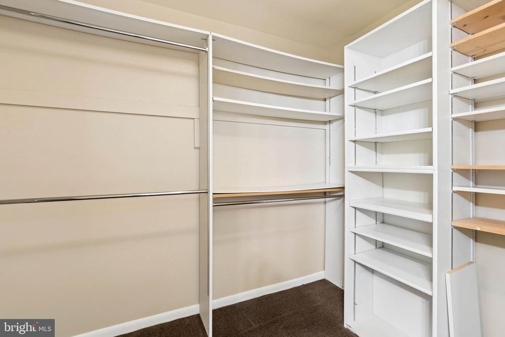 Walk-in closet with hanging rods and extensive white shelving.