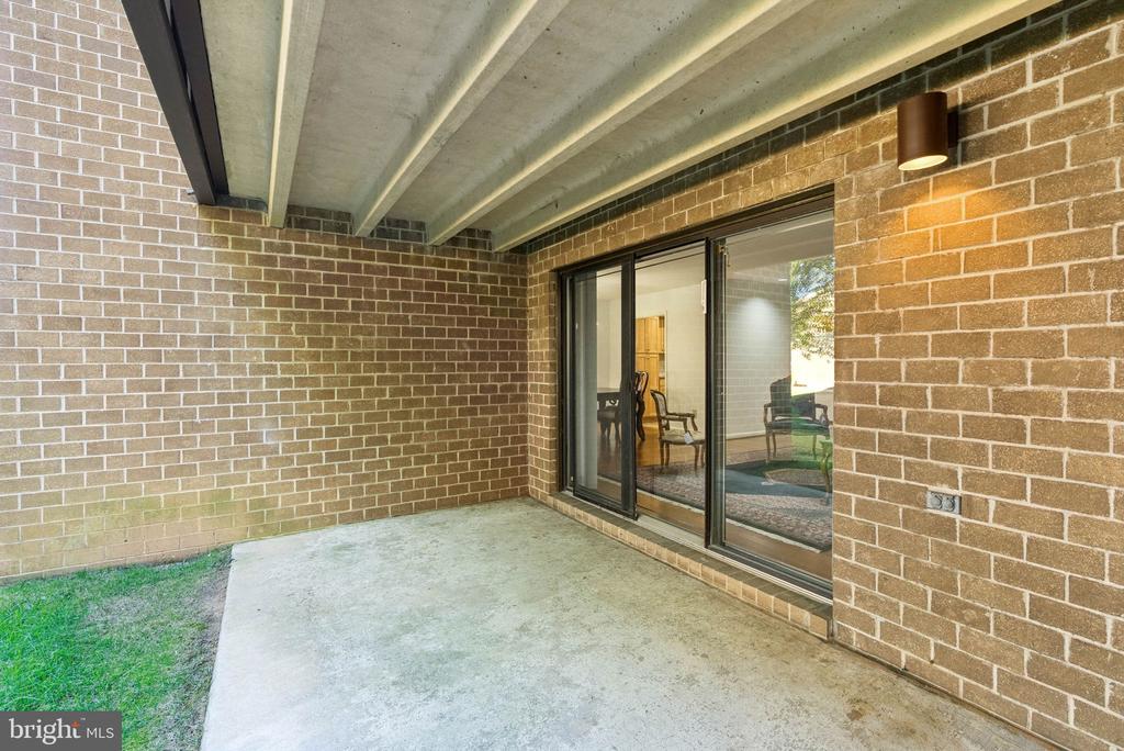 Covered concrete patio with brick walls and sliding glass doors opening into the home.