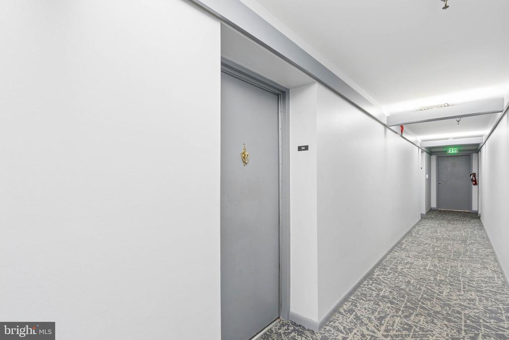 Apartment corridor with gray unit door, patterned carpet, and an EXIT sign.