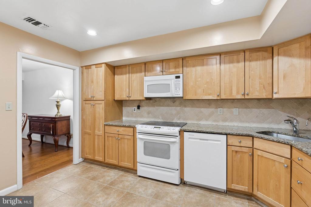 Kitchen with light wood cabinets, granite countertops, white appliances, and a tiled backsplash.