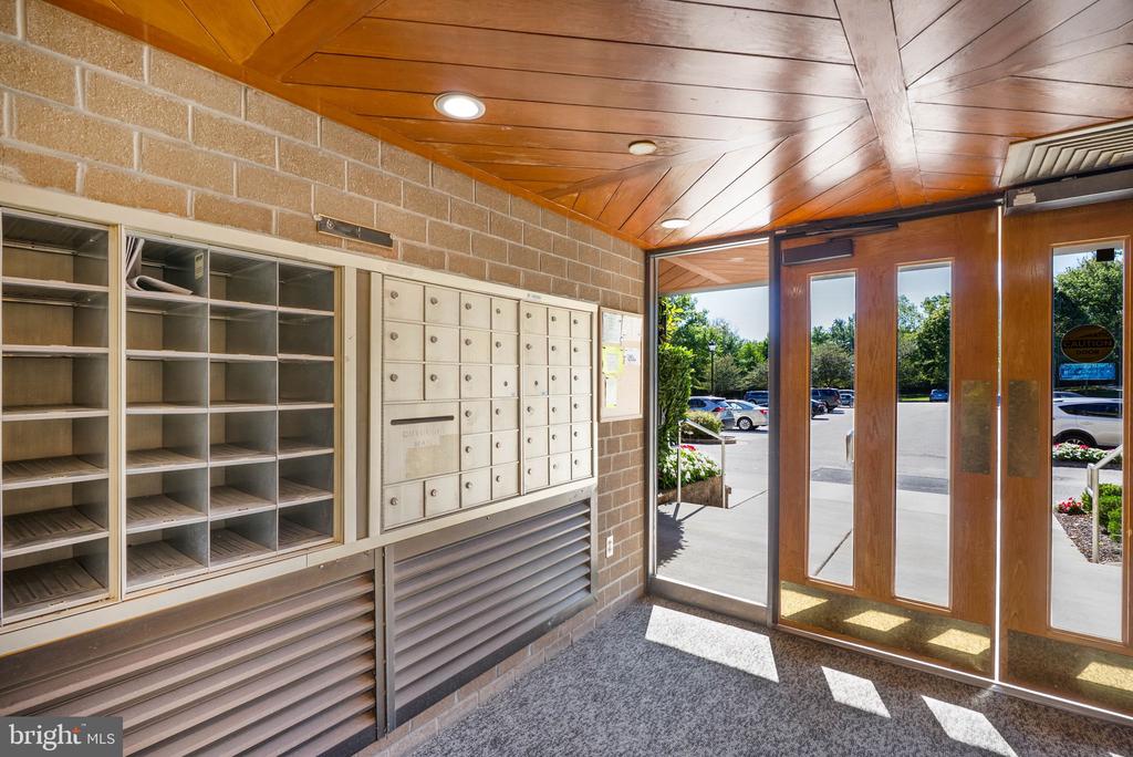 Building entrance mail area with wall-mounted mailboxes, parcel shelves, and glass doors.