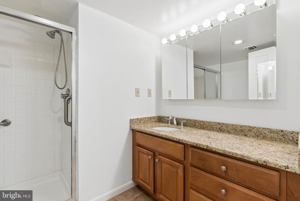 Bathroom with granite vanity, wood cabinetry, mirrored medicine cabinet, and glass-enclosed shower.