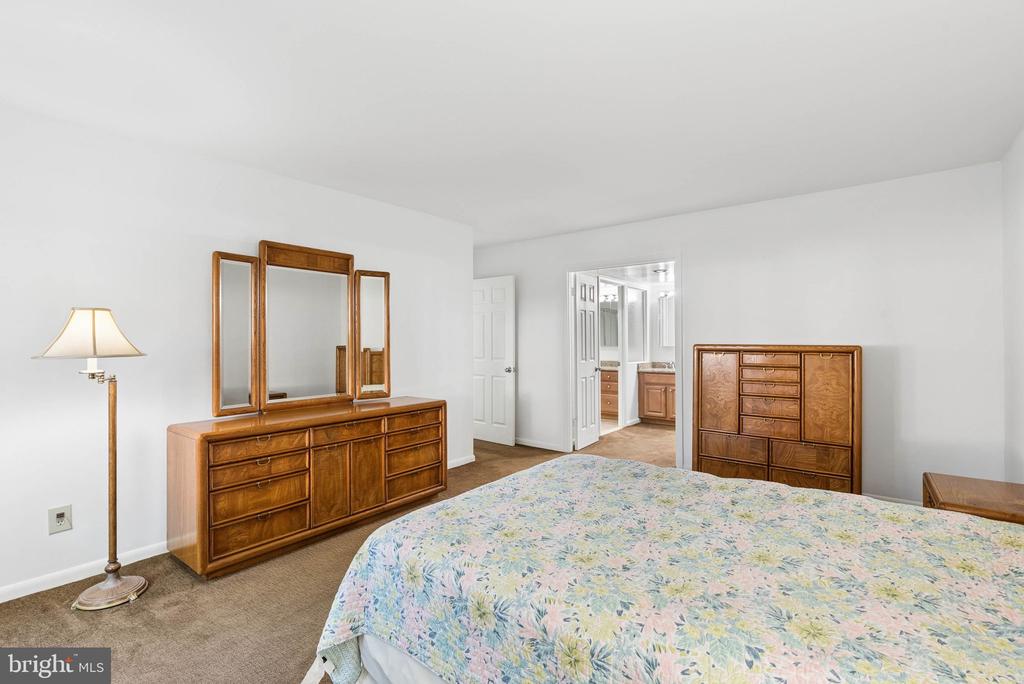 Bedroom with a floral bedspread, wooden dressers, and an open doorway to the bathroom.