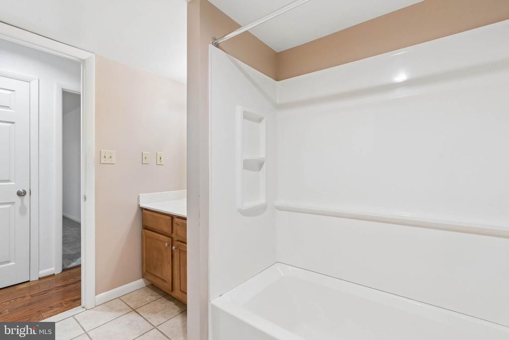 Bathroom with a white tub and shower beside a wood vanity and tiled floor.