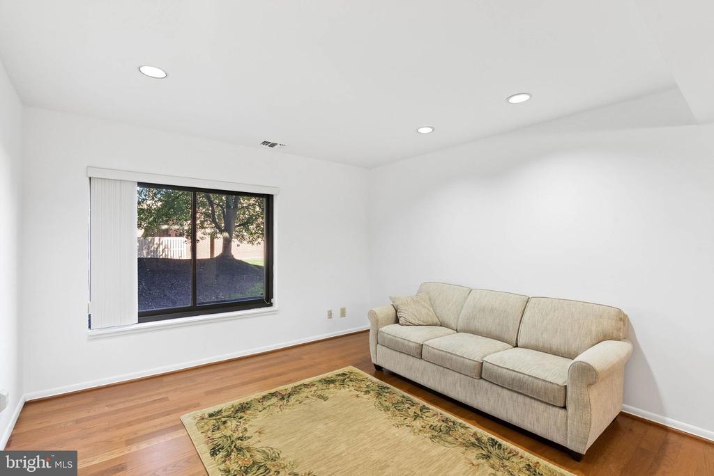 Living room with hardwood floors, a beige sofa, floral rug, and large window with vertical blinds.