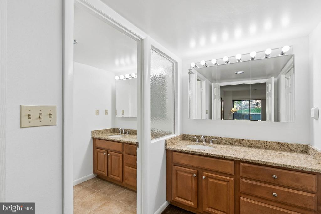 Bathroom with a granite double-sink vanity, wood cabinets, and a separate vanity area.
