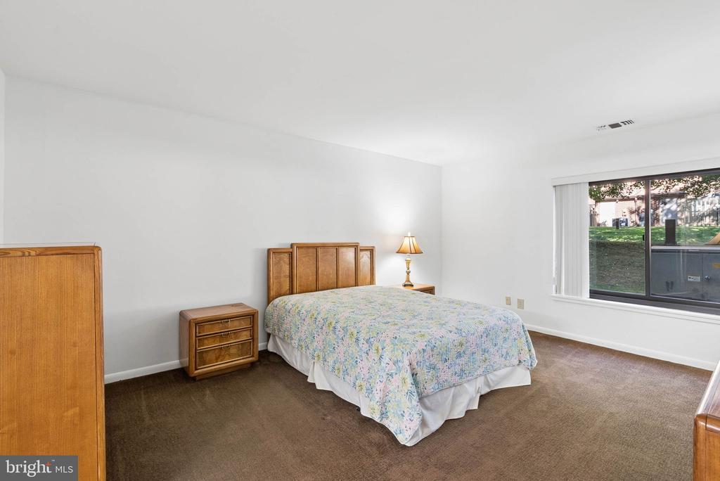 Bedroom with a wooden bed, floral bedspread, brown carpet, and large window overlooking a lawn.