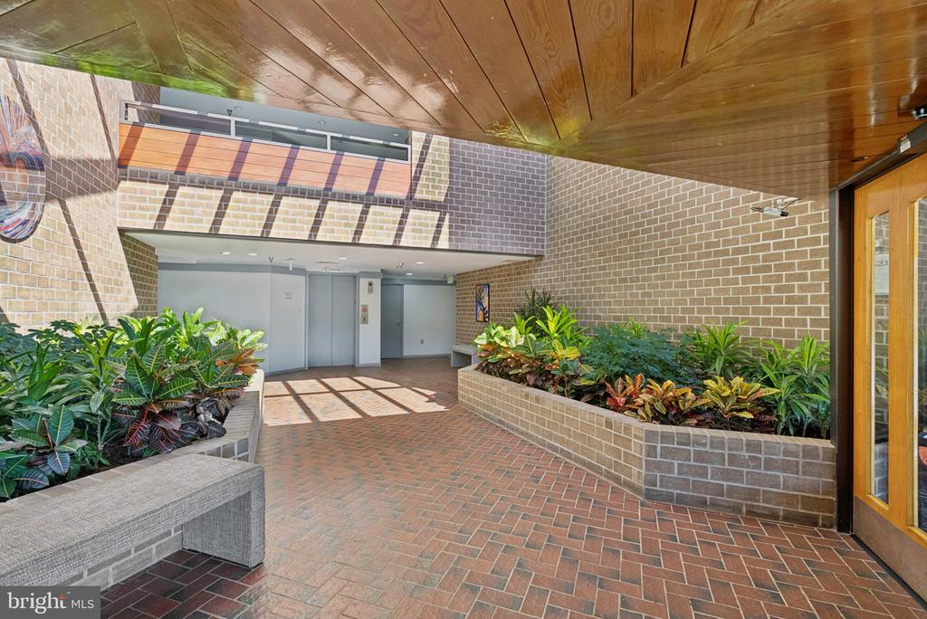 Condominium lobby with elevators, brick flooring, and raised planters beneath a wood-paneled ceiling.