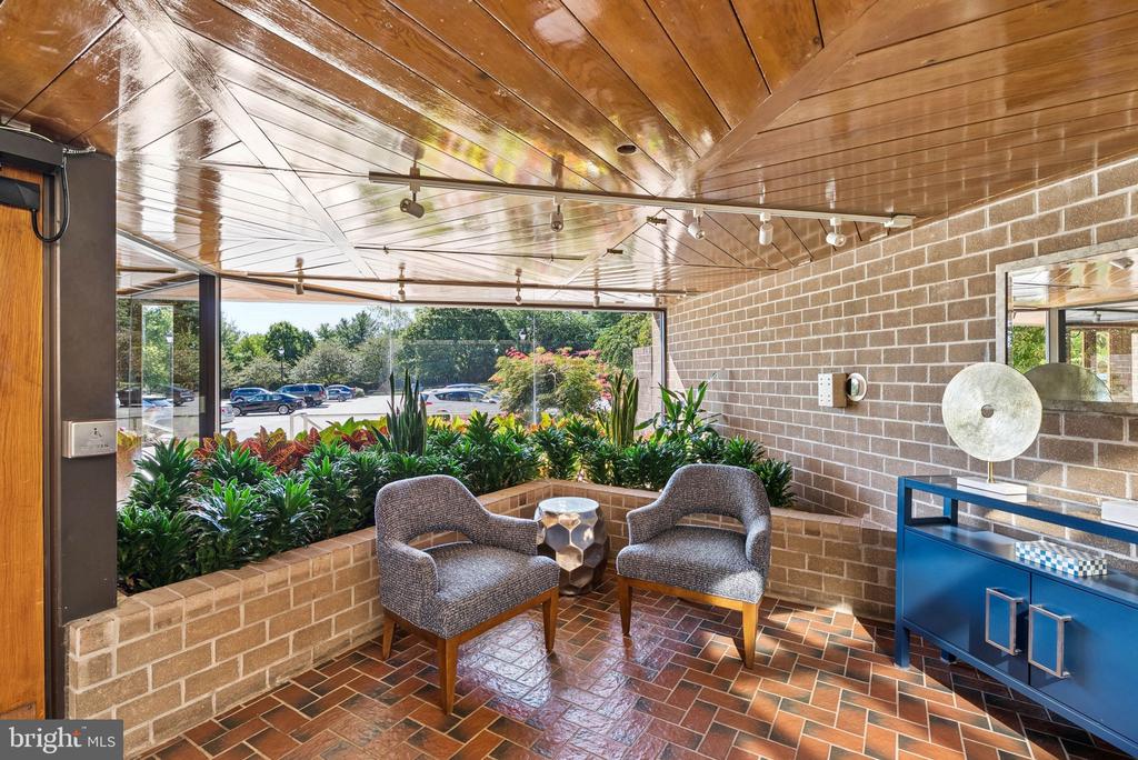Furnished lobby sitting area with two chairs, a wood-paneled ceiling, brick walls, and large windows.