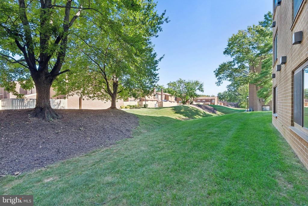 Residential grounds with a broad lawn, mature shade trees, and a brick building.