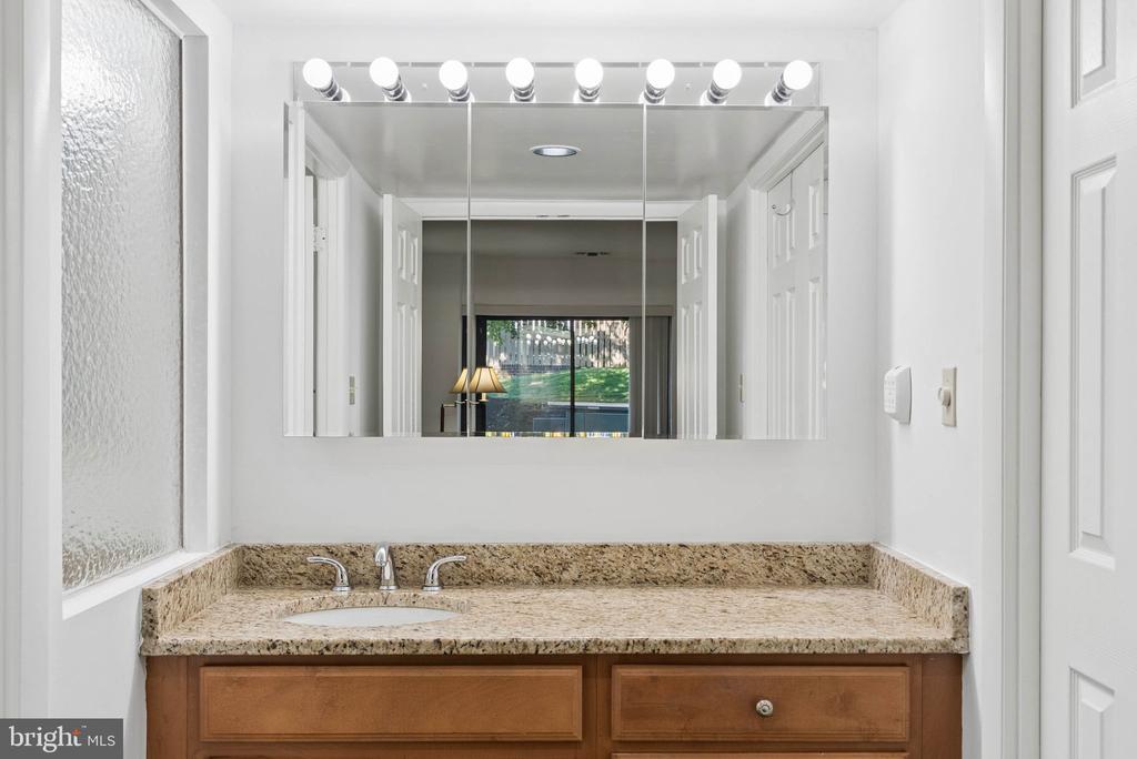 Bathroom vanity with tan granite counters, wood cabinets, and a large mirror with bright lights.