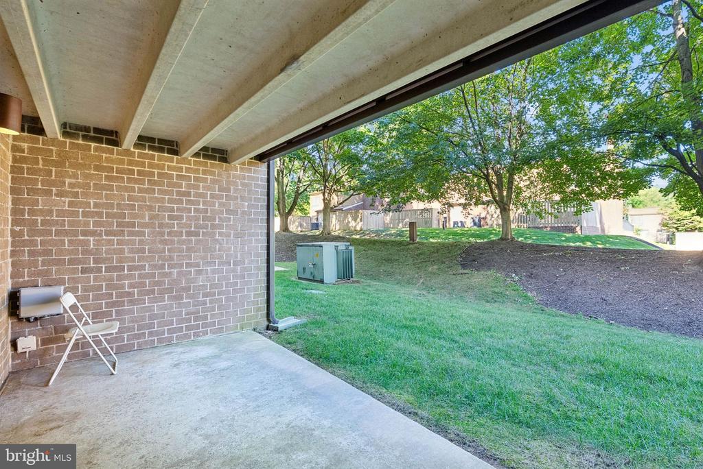 Covered concrete patio overlooking a grassy yard with mature trees.