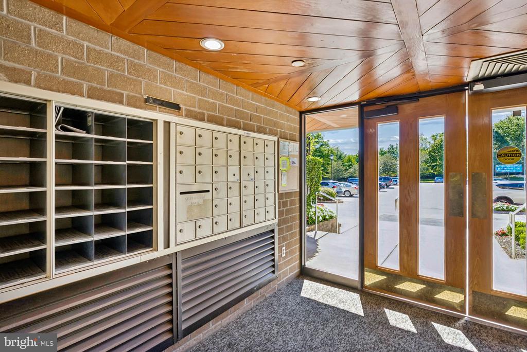 Condominium entry vestibule with mailboxes, open cubbies, and wood-and-glass doors.