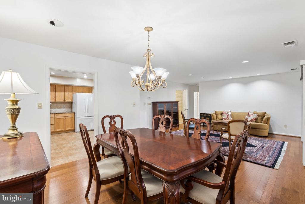 Dining room with a polished wood table, chandelier, and adjoining kitchen and living area.