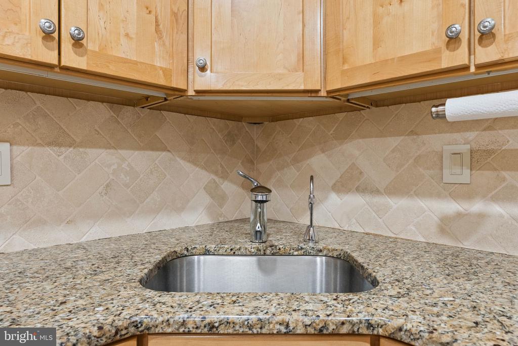 Kitchen sink with granite countertop, light wood cabinets, and beige tile backsplash.