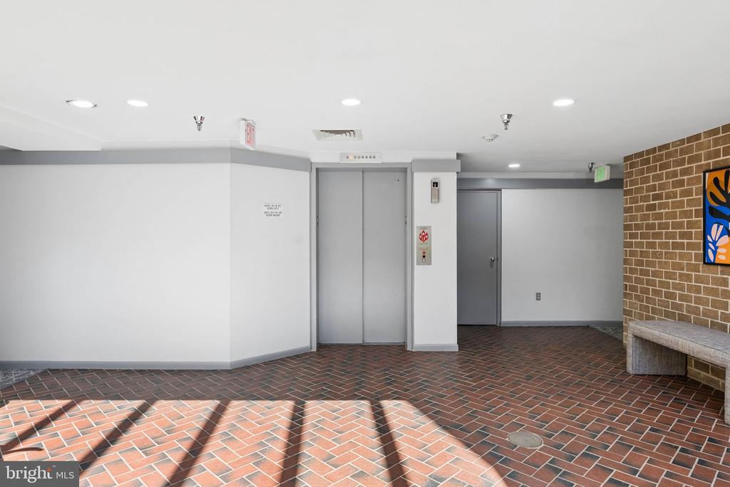 Building lobby with an elevator, brick floor, and bench along a brick wall.