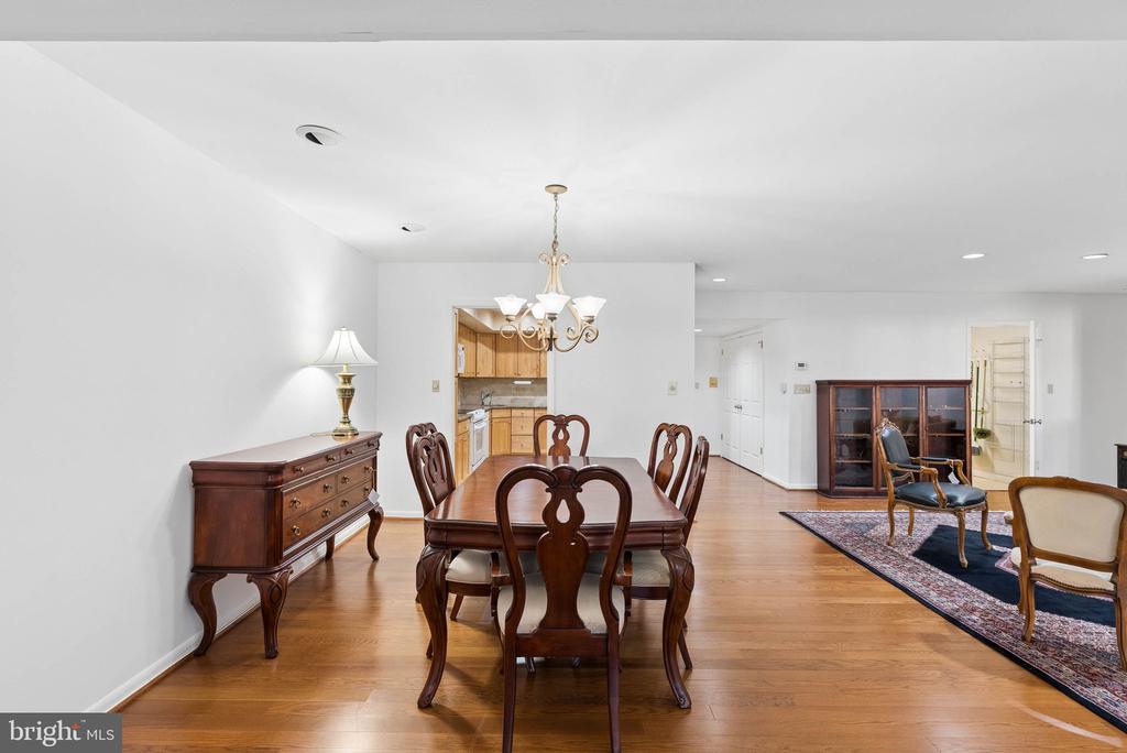 Dining room with a polished wood table, chandelier, and adjoining kitchen and sitting area.