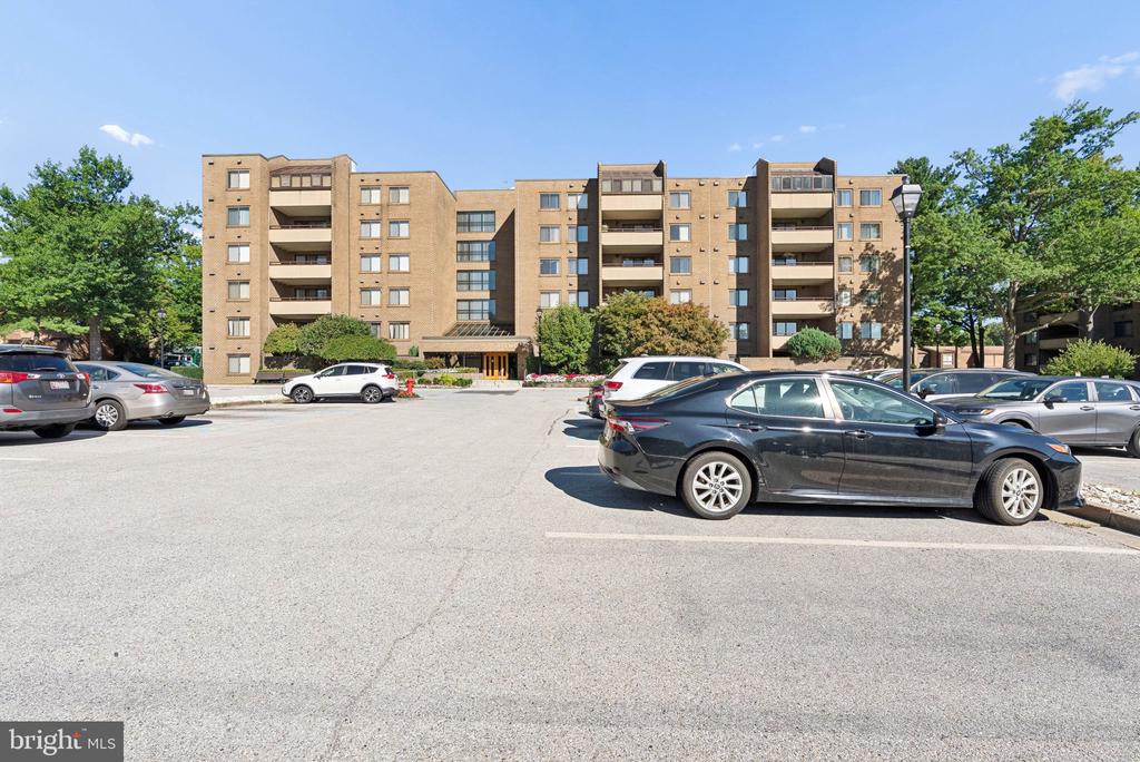 Multi-story tan apartment building with balconies, viewed from its parking lot.